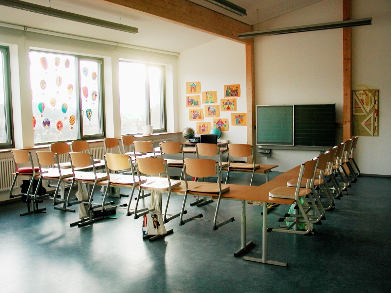 Ein Klassenzimmer mit Tischen, Stühlen und einer grünen Tafel.